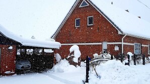 Ein rot backsteins Gebäude mit einem dreieckigen Dach und einer Garage. Schnee türmt sich vor dem Eingang und auf dem Dach.