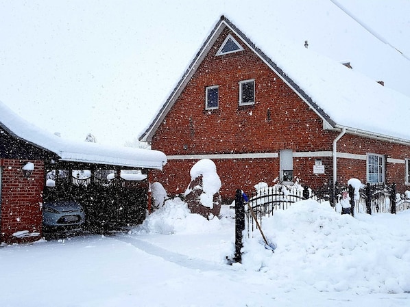 Ein rot backsteins Gebäude mit einem dreieckigen Dach und einer Garage. Schnee türmt sich vor dem Eingang und auf dem Dach.