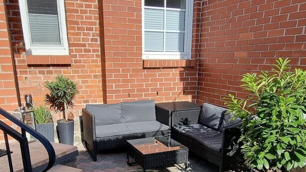 Eine Terrasse mit Korbmöbeln, Blumentöpfen und einer Backsteinmauer.