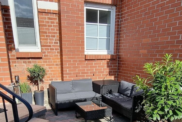 Eine Terrasse mit Korbmöbeln, Blumentöpfen und einer Backsteinmauer.