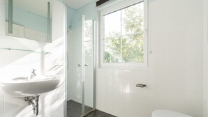 Uma casa de banho moderna com lavatório branco, cabine de duche em vidro, sanita e janela que permite entrada de luz natural.