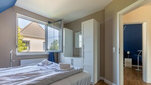 Quarto com uma cama grande, janela, guarda-roupa e banheiro visível por uma porta aberta.