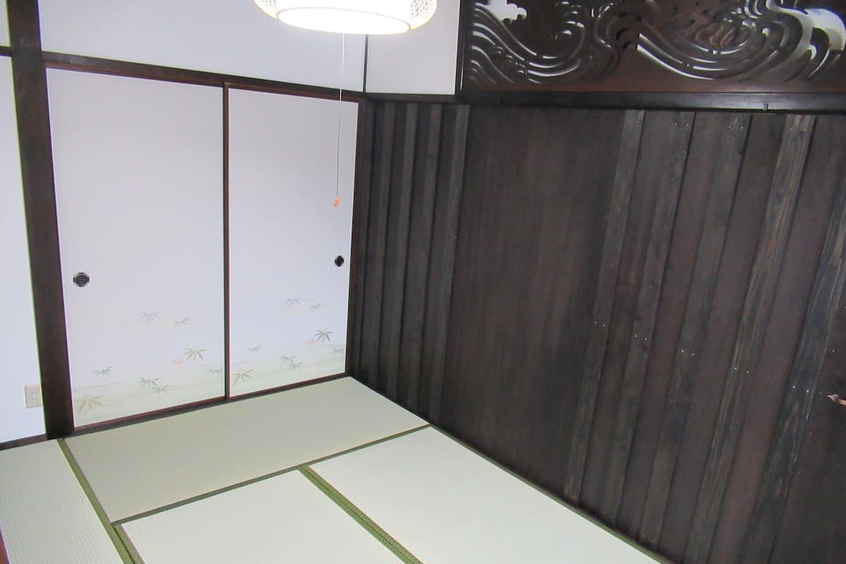 Een traditionele Japanse kamer met tatami vloerbedekking, shoji schermen en een wand van donker hout.
