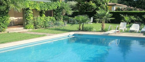 A clear blue swimming pool with lounge chairs and greenery around.