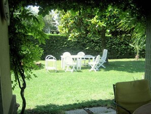 A patio area with a table and chairs, surrounded by lush greenery and a hedge. - Villa in Lazise With Lake Garda Views (Lazise)