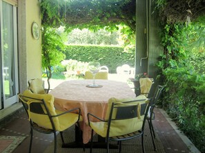 An outdoor dining area with a round table and chairs, surrounded by greenery and a view of a garden. - Villa in Lazise With Lake Garda Views (Lazise)