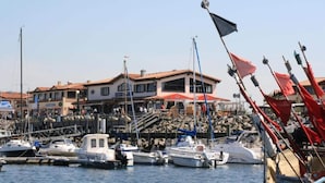 Un puerto deportivo con barcos amarrados, un edificio con toldo rojo y un cielo despejado.