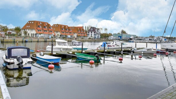 A marina with various boats docked, a building with red roofs, and calm water reflecting the sky. - Apartment in Wiek auf Rgen With Forest (Wiek)