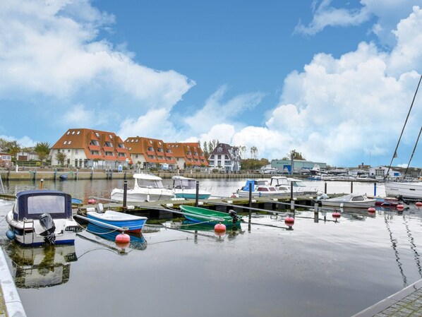 Uma marina com vários barcos atracados, um edifício com telhados vermelhos e água calma refletindo o céu.