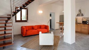 Et moderne interiør med trappe, orange sofa, hvid stol, køkkenafsnit og spisebord.