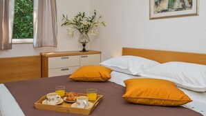 Un letto rifatto con due cuscini, un comodino con un vaso di fiori e un vassoio con prodotti per la colazione.