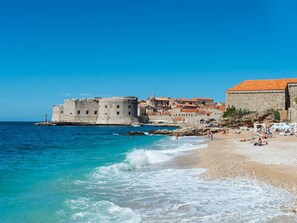Eine Küstenstadt mit einer historischen Festung am Meer, einem Sandstrand und klarem, blauem Wasser.