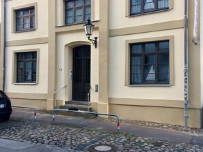 A building with a beige facade, multiple windows, a black door, and a metal railing in front.
