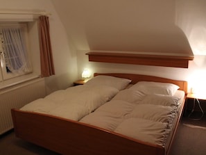 A single bed with a wooden headboard in a room with a sloped ceiling and a window with curtains. - Wohnung mit Garten in Klutz (Klütz)