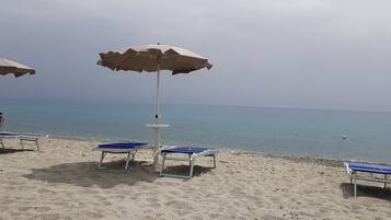 Una playa con varias tumbonas y sombrillas, una orilla arenosa y el mar al fondo.