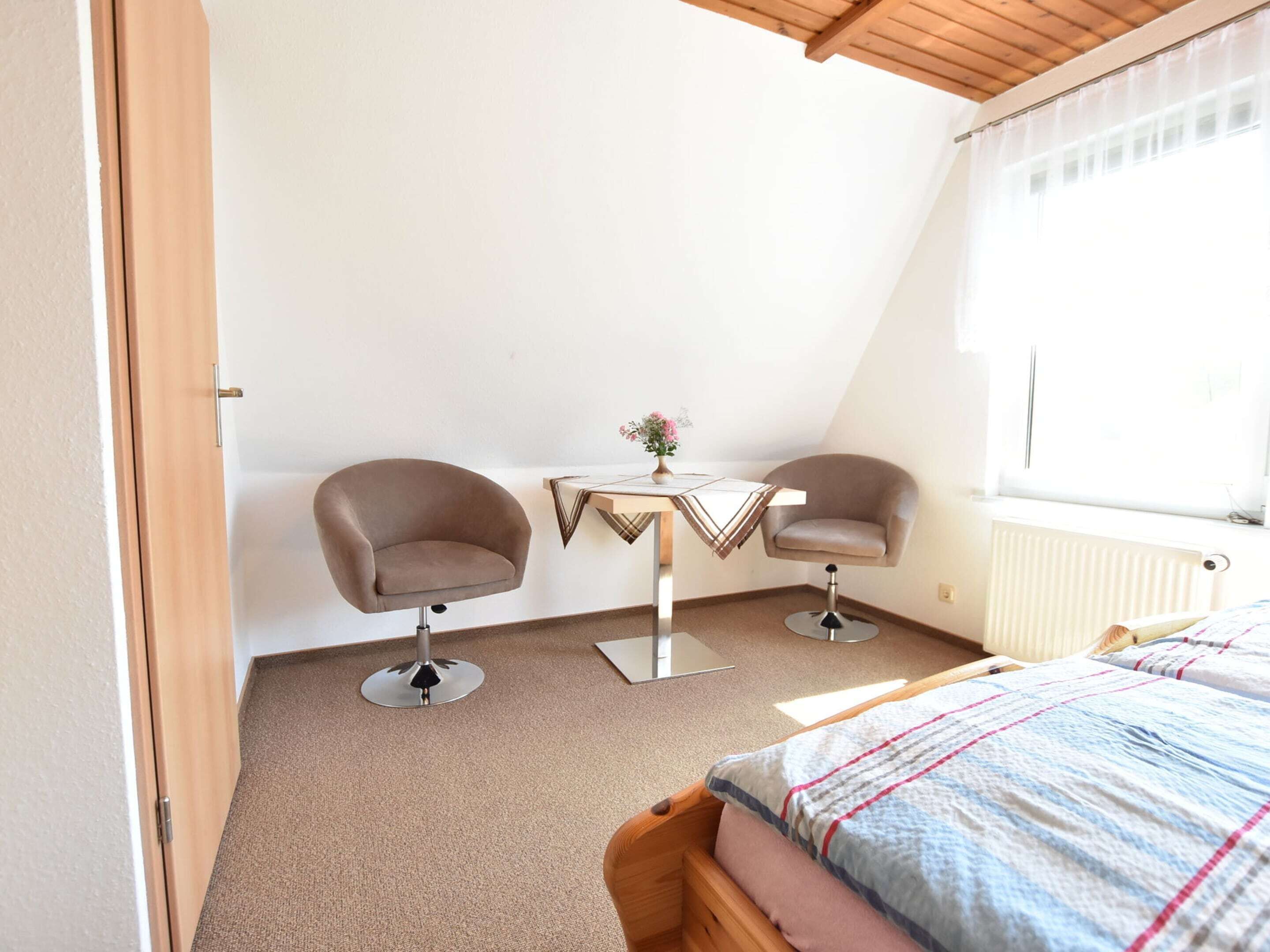 A bedroom with a bed, two armchairs, a small table with a vase, and a window.
