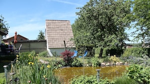 A garden with a pond, a tall building, and a tree. - Apartment in Pepelow for Zwei Personen (Am Salzhaff)