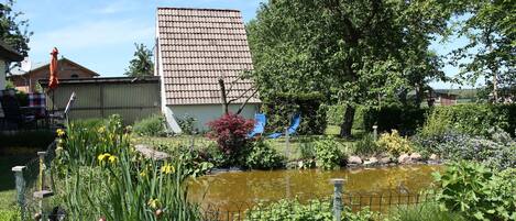 A garden with a pond, a tall building, and a tree.