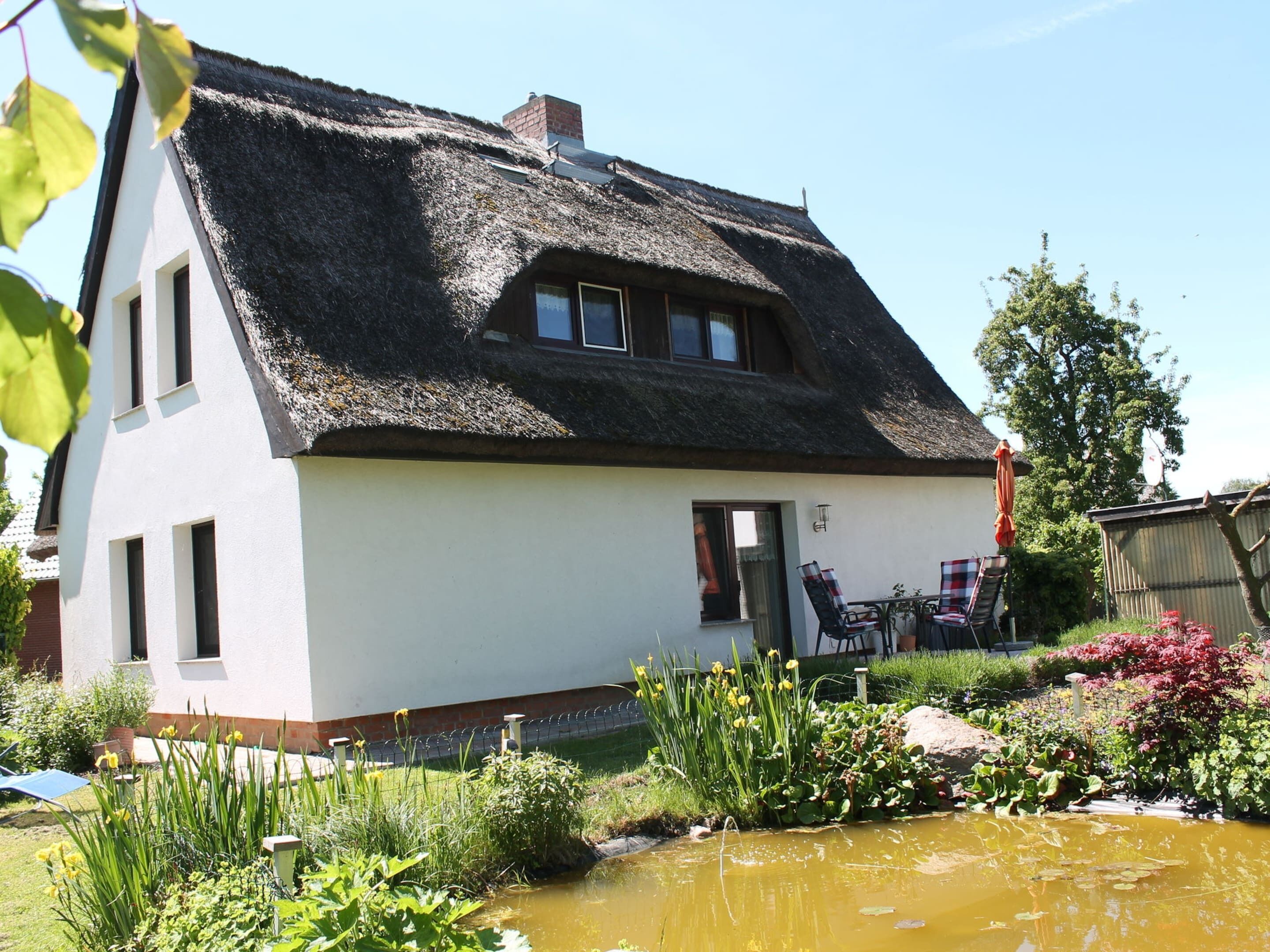 Ein Haus mit einem Strohdach, ein kleiner Garten mit Teich und ein Stuhl davor.
