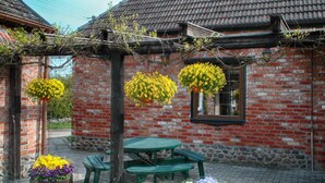 A rustic brick building with a tiled roof, a green wooden table, and benches. There are flower baskets on the ground. - Apartment in a Stylish House in the Countryside Near the Sea (Darlowo)