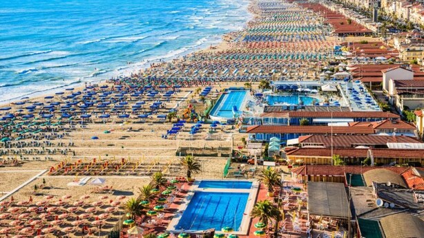 Un resort costero con varias piscinas, sombrillas de playa y un extenso paseo marítimo frente al mar.