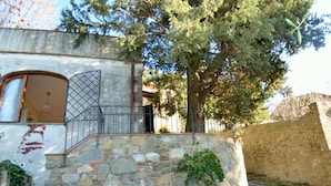 Un edificio de paredes de piedra con una verja metálica, una puerta de madera y un gran árbol en primer plano.