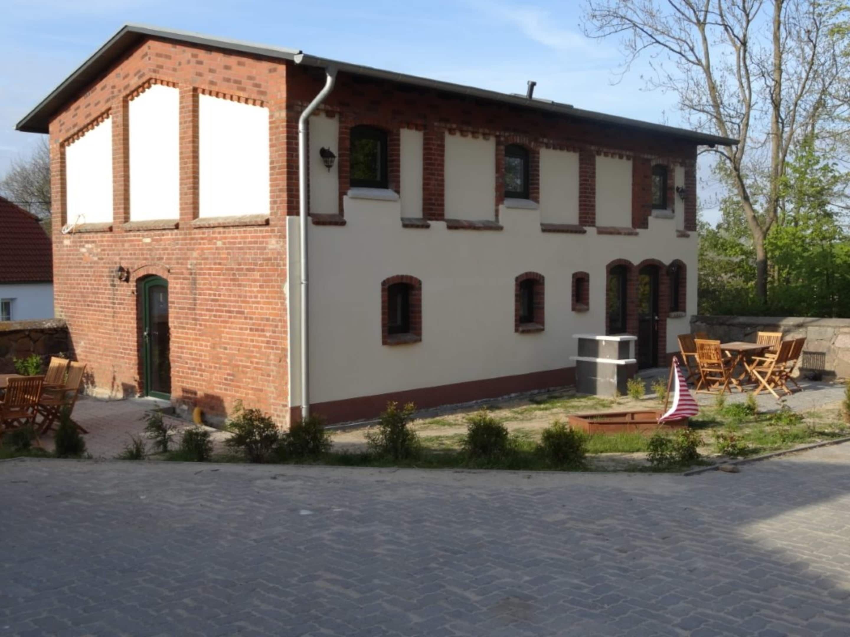 Ein zweistöckiges Gebäude mit Backsteinfassade und weißen Wänden. Es gibt eine Terrasse mit Gartenmöbeln und eine kleine amerikanische Flagge.