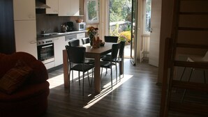 A modern kitchen with white cabinets, a dining table with chairs, and a view of the outdoors through a glass door. - Country House Near Baltic Sea Beach (Bastorf)
