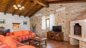 A rustic living room with a stone wall, wooden beams, a fireplace, a sofa, a television, and a coffee table. - Elegant Villa in Istria With Outdoor Pool (Tinjan)