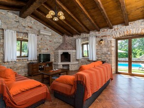 A rustic room with stone walls, a fireplace, wooden furniture, and a view of a swimming pool. - Elegant Villa in Istria With Outdoor Pool (Tinjan)