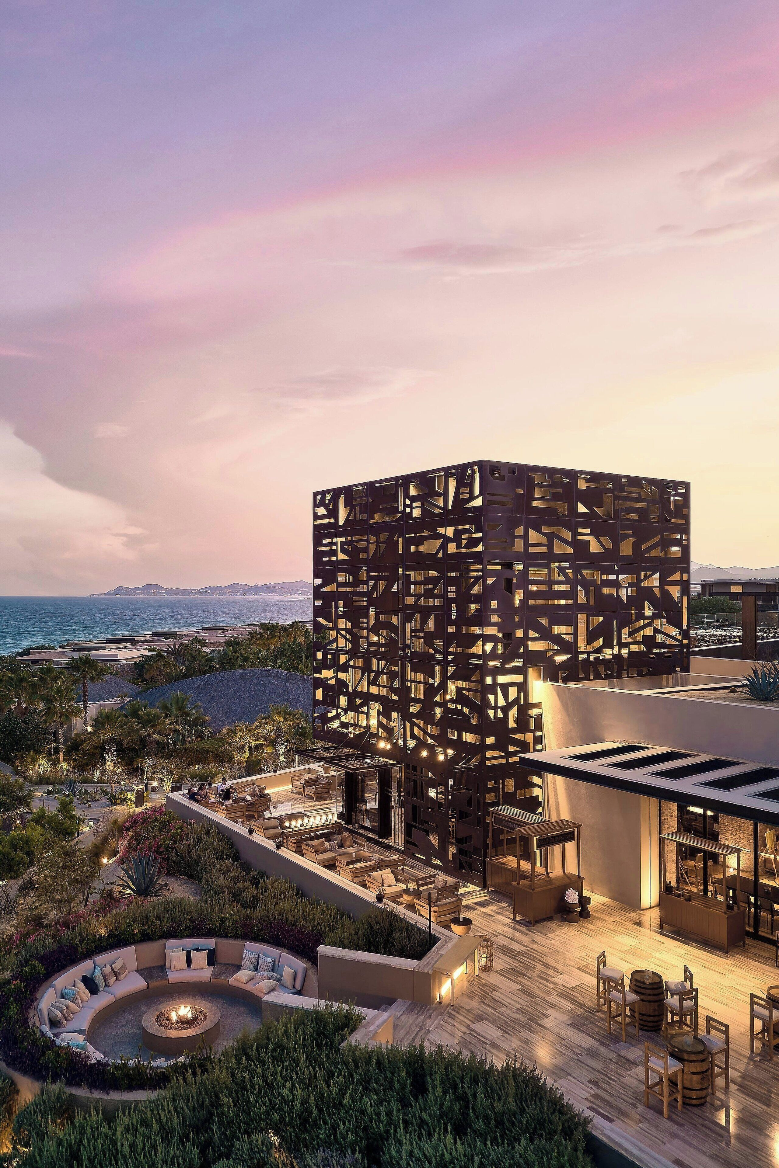A rooftop terrace with a circular seating area, a fire pit, and a view of the sea and mountains.