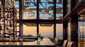A bar area with a large window, hanging lights, and a view of the cityscape. - Zadun Los Cabos, a Ritz-Carlton Reserve Residence (San José del Cabo)