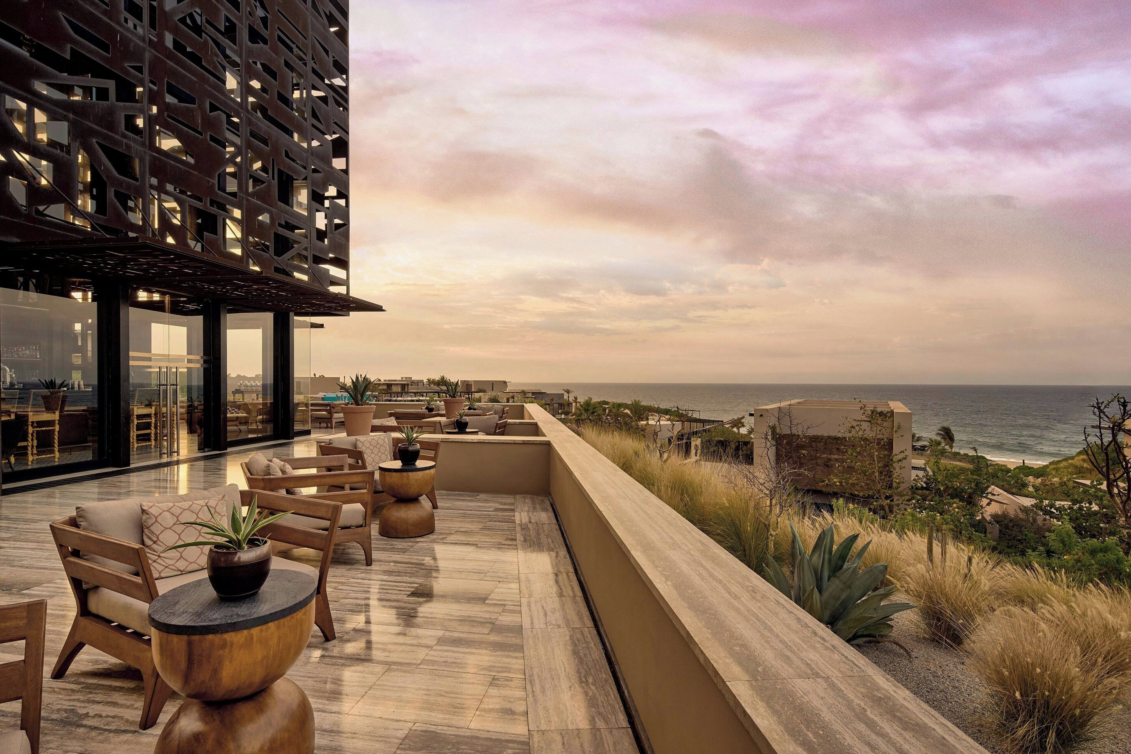 A rooftop terrace with outdoor seating, a view of the ocean, and a modern building with a geometric facade.