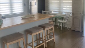 A kitchen with wooden bar stools, a refrigerator, and a dining table with chairs. - Our Little Piece of Heaven (Edisto Island)