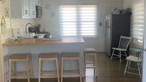 A compact kitchen with wooden countertops, a built-in microwave, and a refrigerator. There are four wooden stools and a window with blinds. - Our Little Piece of Heaven (Edisto Island)