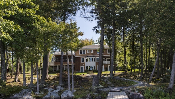 A two-story building with a deck overlooking a river, surrounded by trees. - Luxury Family Home / Retreat Center on Great Pond (Belgrade)