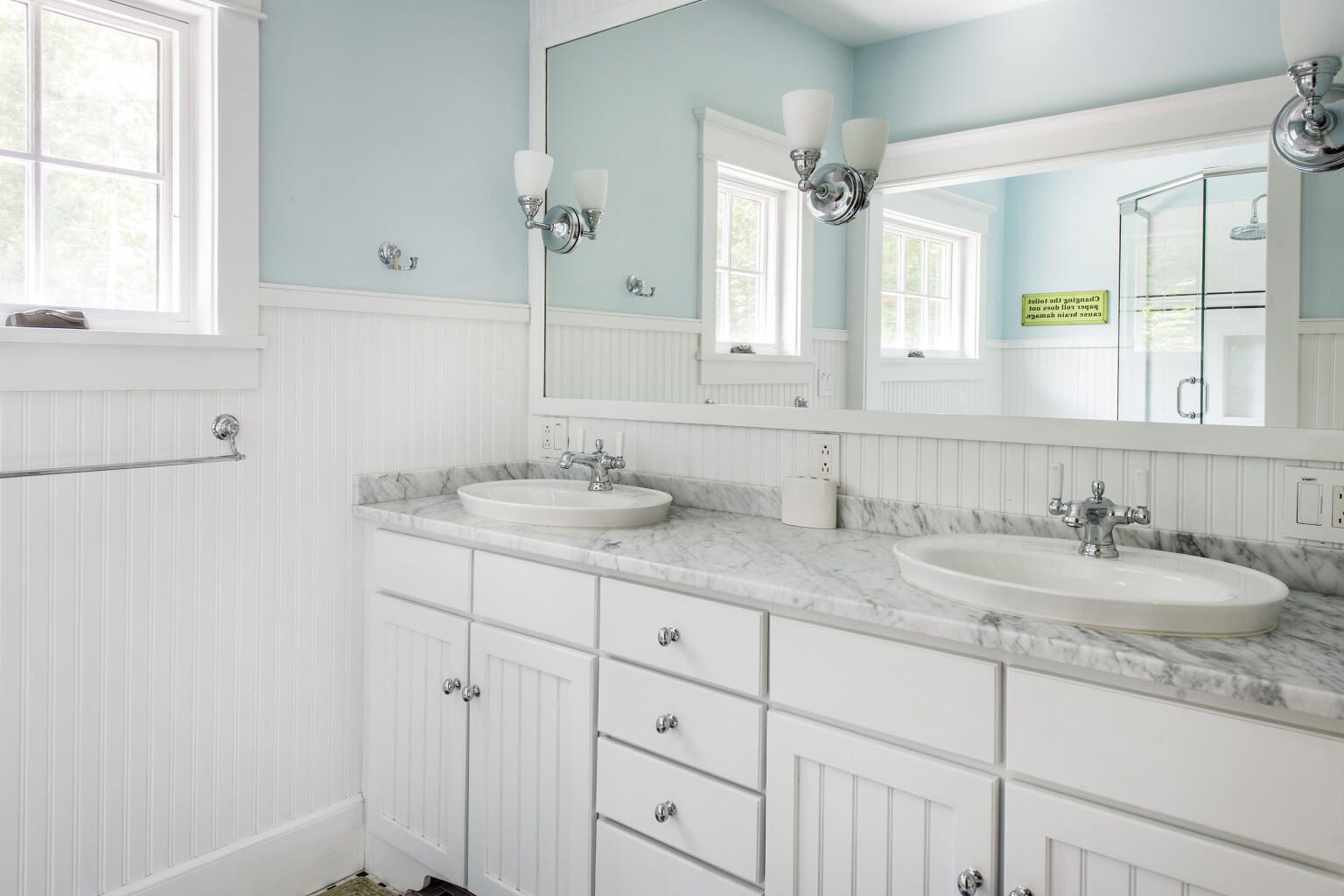 A bathroom with two sinks, white cabinetry, and a large mirror with wall sconces.