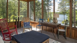 A wooden deck with a table, chairs, and a view of a lake surrounded by trees. - Luxury Family Home / Retreat Center on Great Pond (Belgrade)