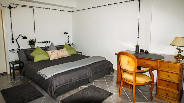Quarto com cama, escrivaninha, cadeira e duas luminárias.