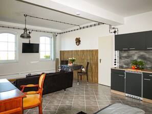 Eine moderne Küche mit dunklen Schränken, ein Essbereich mit einer schwarzen Couch und Holzsesseln, ein gefliester Boden und ein Fenster, das für natürliches Licht sorgt.