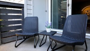 Two black wicker chairs with metal legs on a small table, a potted plant, and a glass door leading inside. - Stylish, New & Clean 1b apt w/ King Bed+Pool+Gym+Parking (Beaverton)
