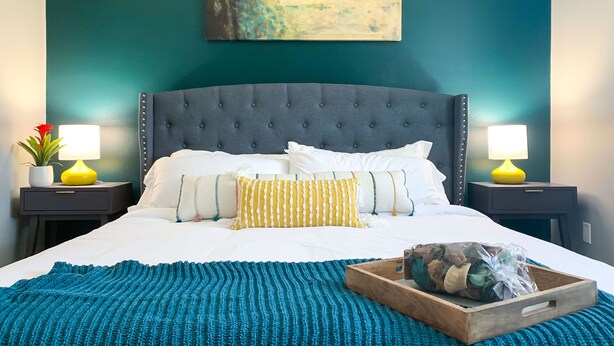 A neatly made bed with white linens, a teal knitted blanket, and a wooden tray with a wrapped item. - Stylish, New & Clean 1b apt w/ King Bed+Pool+Gym+Parking (Beaverton)