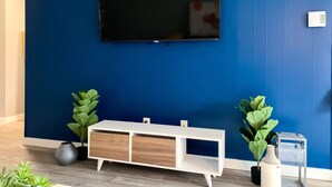 A room with a blue wall, a mounted TV, a white console table, and two potted plants. - Stylish, New & Clean 1b apt w/ King Bed+Pool+Gym+Parking (Beaverton)