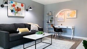 A modern living room with a black sofa, a white coffee table, a desk, and a bookshelf. - Stylish, New & Clean 1b apt w/ King Bed+Pool+Gym+Parking (Beaverton)