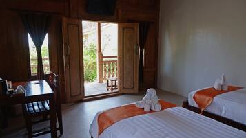 A hotel room with two beds, a wooden desk, and a balcony with a view of greenery.