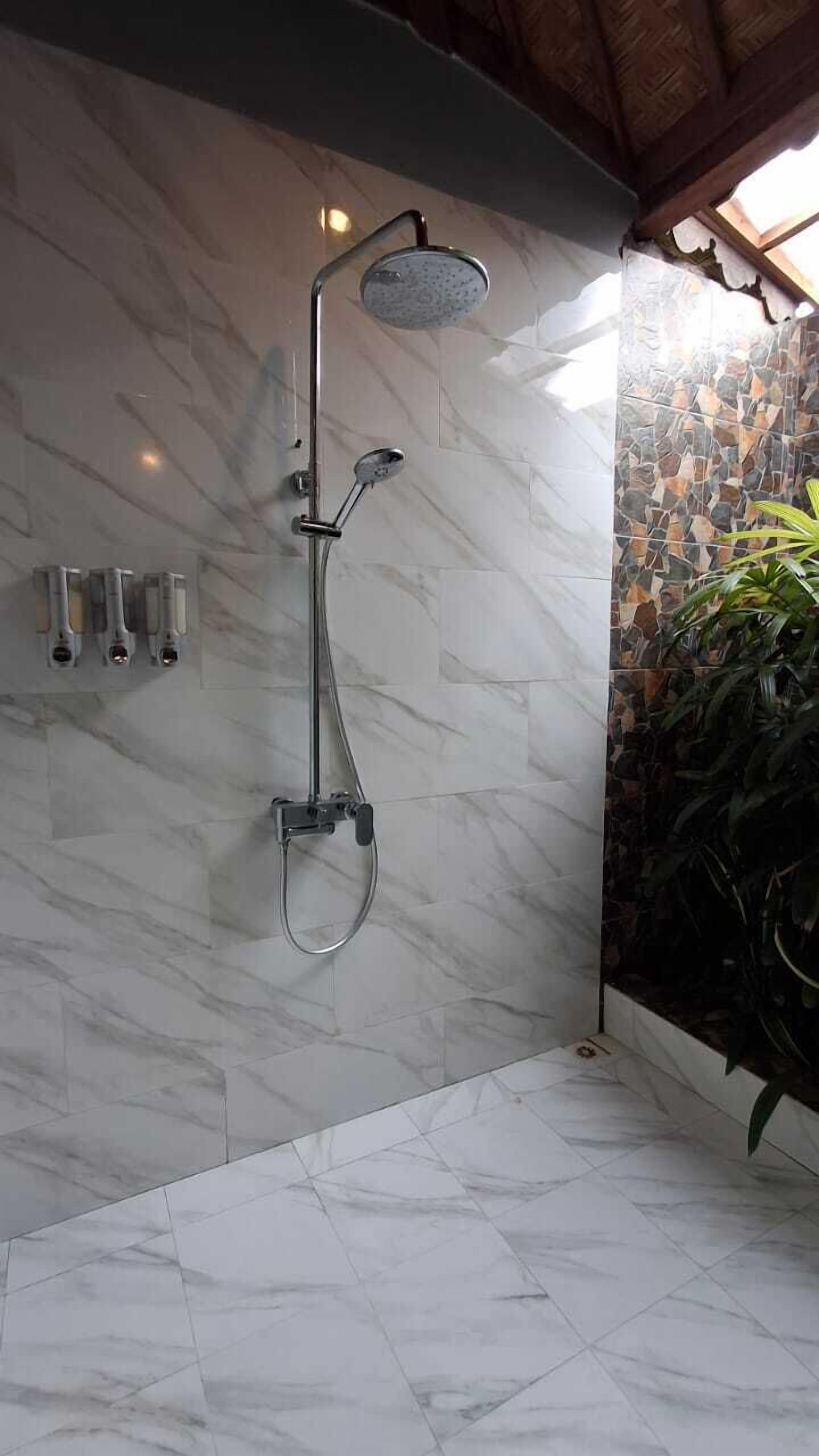 Una ducha con cabezal de ducha tipo lluvia y cabezal de ducha manual, pared de mármol y suelo de baldosas.