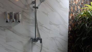 Una ducha con cabezal de ducha tipo lluvia y cabezal de ducha manual, pared de mármol y suelo de baldosas.