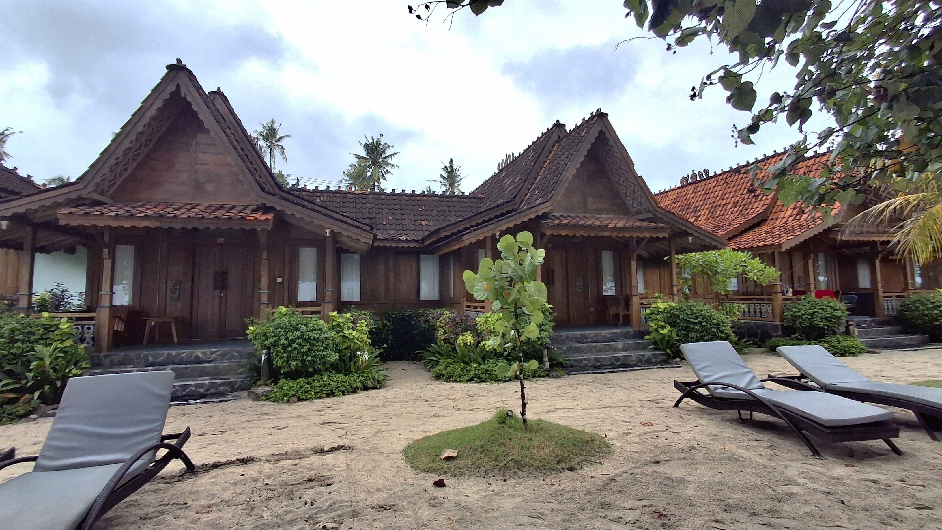 A traditional wooden building with a tiled roof, surrounded by a sandy area with lounge chairs.