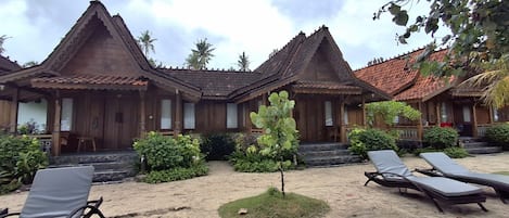 A traditional wooden building with a tiled roof, surrounded by a sandy area with lounge chairs.