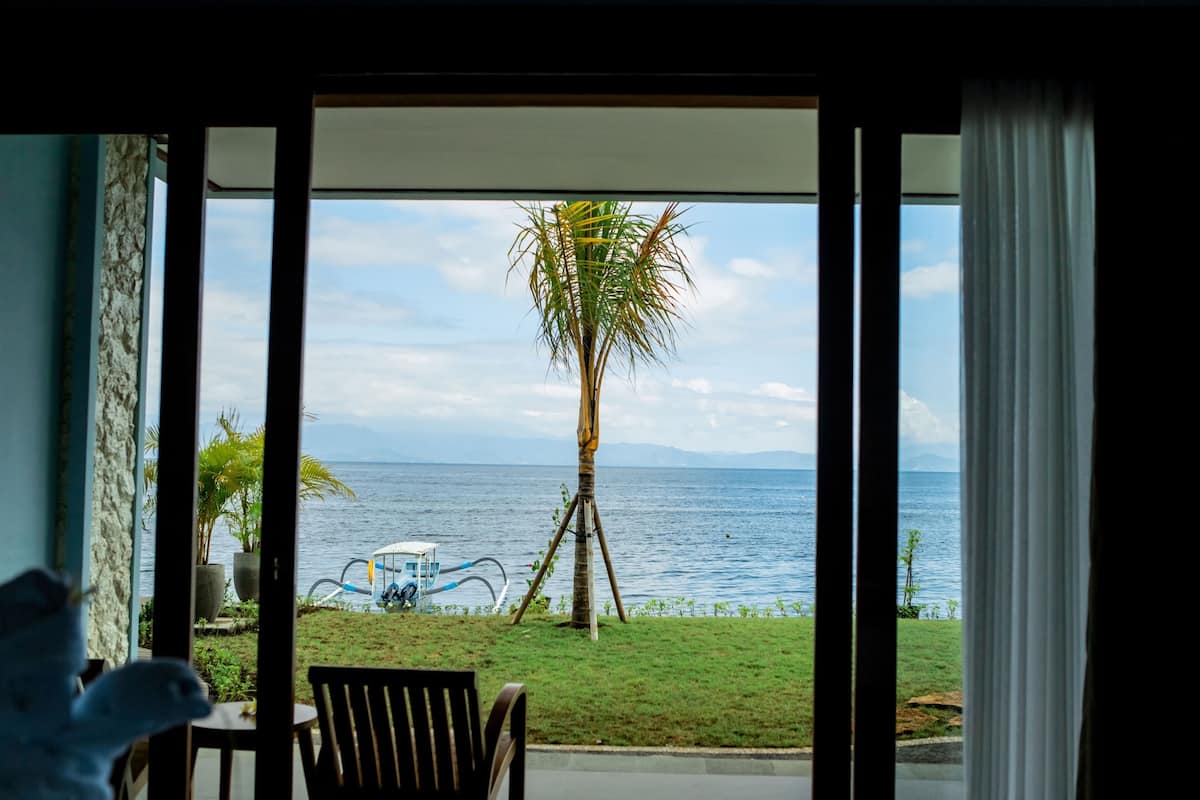 A room with a view of a palm tree and the sea through an open door.